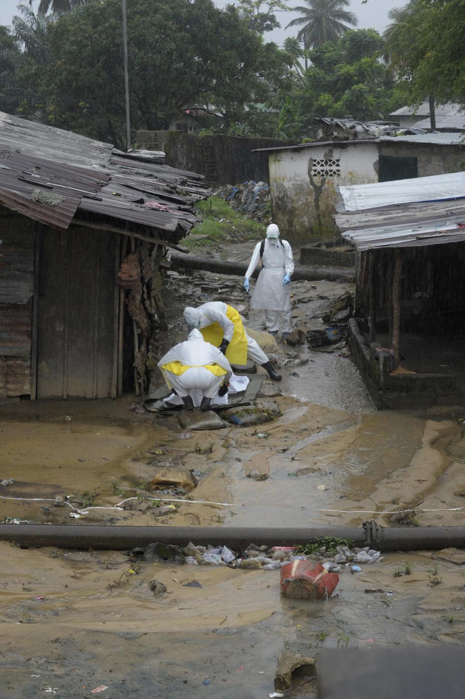 Health workers wearing protective clothing prepare to carry an abandoned dead body presenting with Ebola symptoms at Duwala market in Monrovia August 17, 2014. To try to control the Ebola epidemic spreading through West Africa, Liberia has quarantined remote villages at the epicentre of the virus, evoking the "plague villages" of medieval Europe that were shut off from the outside world. REUTERS/2Tango (LIBERIA - Tags: HEALTH DISASTER)