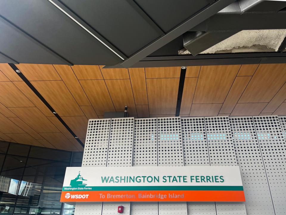 A gray sign with green text saying "Washington State Ferries" with an orange section with metallic "to Bremerton, Bainbridge Island" text
