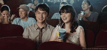 Joseph Gordon-Levitt and Zooey Deschanel in a movie theater, smiling and holding drinks, from the film "500 Days of Summer."