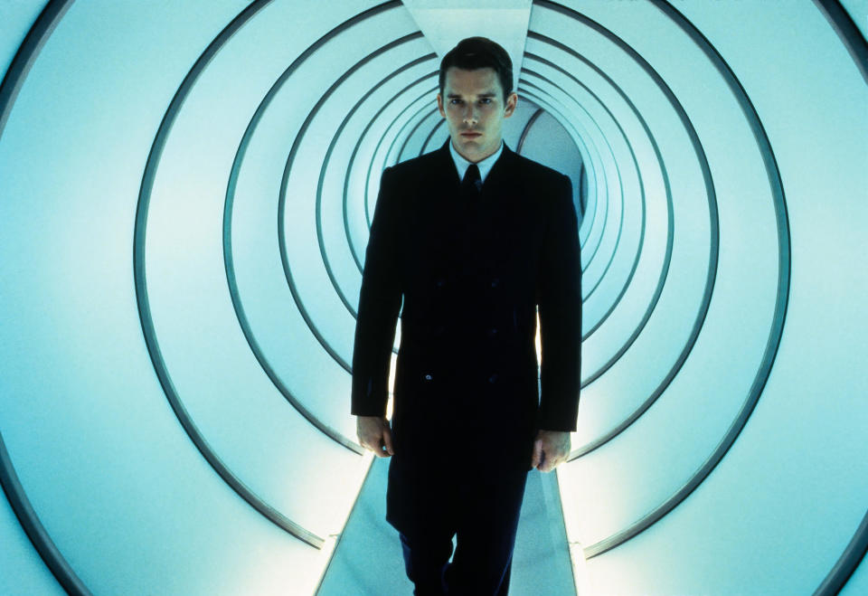 A man in a black suit walks down a brightly lit and futuristic looking tunnel