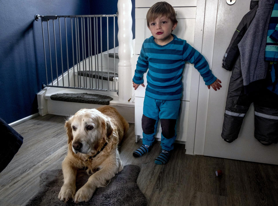 Three year old Oskar, who suffers from a very rare gene defect, stands next to dog Bruno in Eisemroth, central Germany, Thursday, March 25, 2021. One year into the coronavirus pandemic, Katja Heimann is still trying to keep her spirits up - despite several lockdowns and months of teaching seven of her children in home schooling. (AP Photo/Michael Probst)