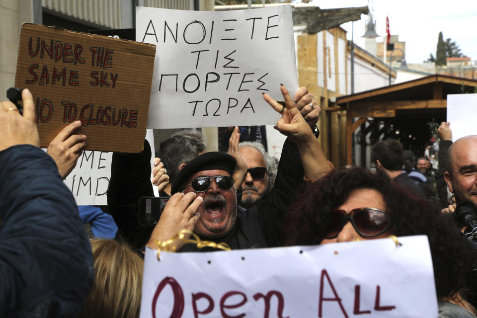 A protestor shouts slogans holding a banner reading in Greek "Open the doors now" during a demonstration against the closing of a crossing point straddling a United Nations-controlled buffer zone in divided capital Nicosia, Cyprus, Saturday, Feb. 29, 2020. Around 200 people gathered at the Ledra Street crossing point to voice their opposition to its closing. The Cyprus government said it closed the Ledra Street crossing point along with three others to help with efforts to prevent the possible spread of a new COVID-19 virus either to the breakaway, Turkish Cypriot north or the internationally recognized, Greek Cypriot south. (AP Photo/Petros Karadjias)