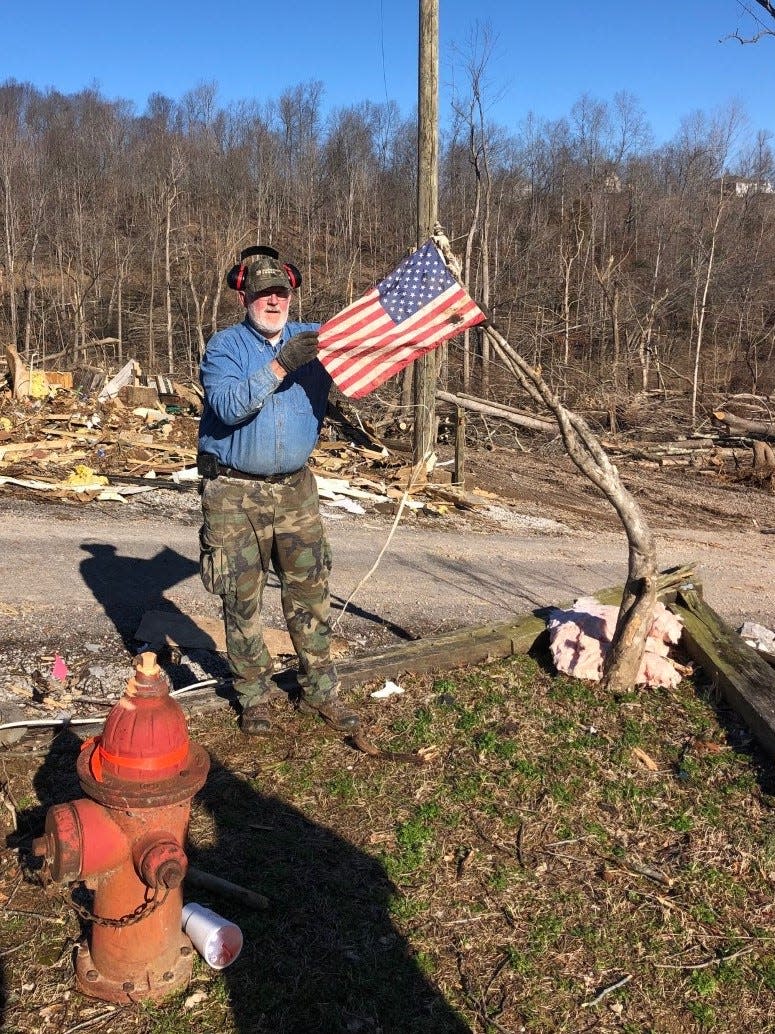 Charlie Snelling hangs a small American flag he found while clearing debris at the site of a home destroyed by a tornado.