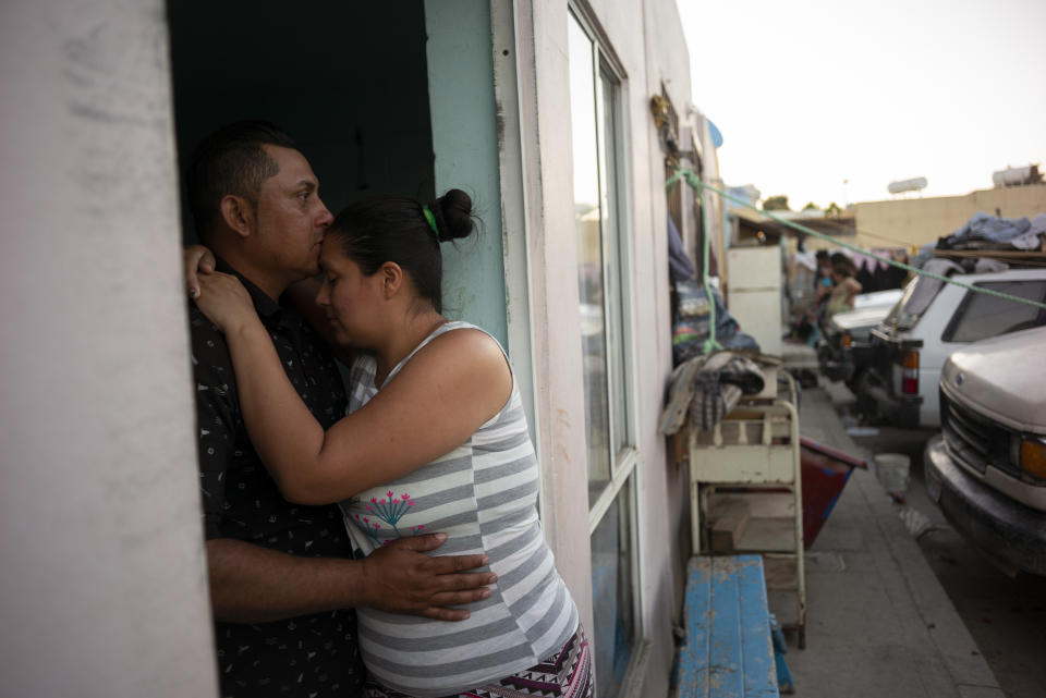 In this June 19, 2019, photo, Juan Carlos Perla, left, embraces his wife, Ruth Aracely Montoya in the entrance to their home in Tijuana, Mexico. The Perla family of El Salvador has slipped into a daily rhythm in Mexico while they wait for the U.S. to decide if they will win asylum. A modest home replaced the tent they lived in at a migrant shelter. (AP Photo/Gregory Bull)