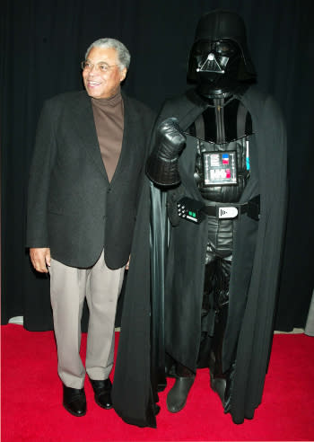 James Earl Jones smiles as he stands next to Darth Vader.