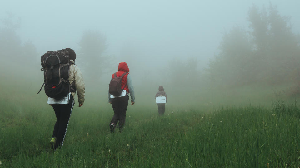 Family hiking with child with backpacks in foggy forest