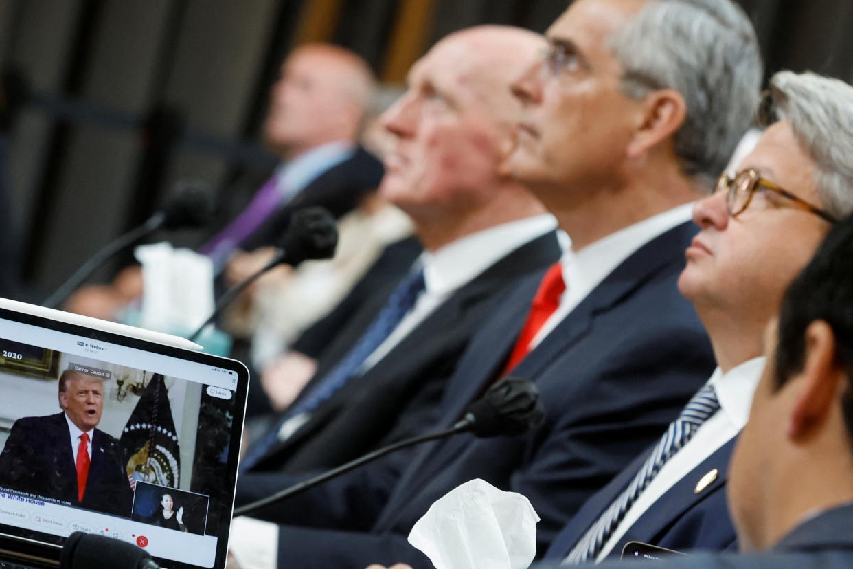 Rusty Bowers, Brad Raffensperger and Gabriel Sterling listen as a laptop shows former U.S President Donald Trump talking in front of a flag.