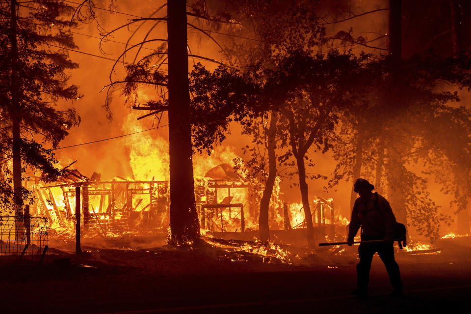 FILE - A firefighter passes a burning home as the Dixie Fire flares in Plumas County, Calif., July 24, 2021. Tens of millions of people are being uprooted by natural disasters due to the impact of climate change, though the world has yet to fully recognize climate migrants or come up with a formalized mechanism to assess their needs and help them. (AP Photo/Noah Berge, File)