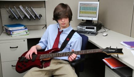 Young millenial office worker goofing off playing a bass guitar in his cubicle