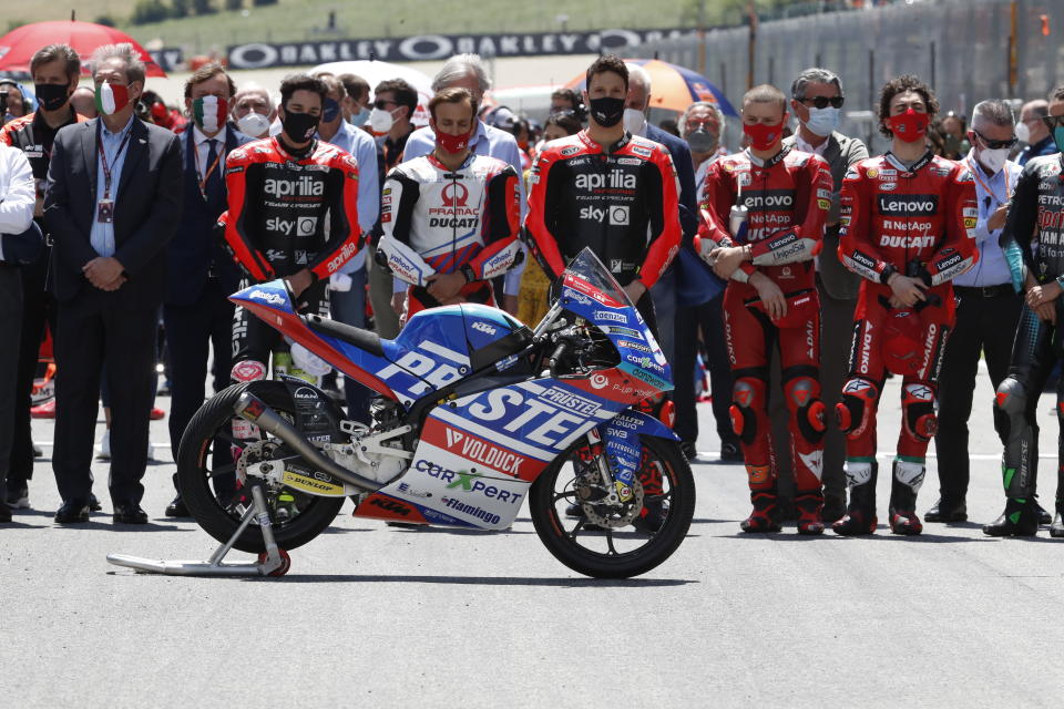 Teammates of 19 years-old Swiss pilot Jason Dupasquier and pilots from other teams stand near his motorbike as they pay a minute of silence in his memory prior to the start of the Motogp Grand Prix of Italy at the Mugello circuit, in Scarperia, Italy, Sunday, May 30, 2021. Dupasquier died Sunday after being hospitalized Saturday, at the Florence hospital following his crash during the qualifying practices of the Moto3. (AP Photo/Antonio Calanni)