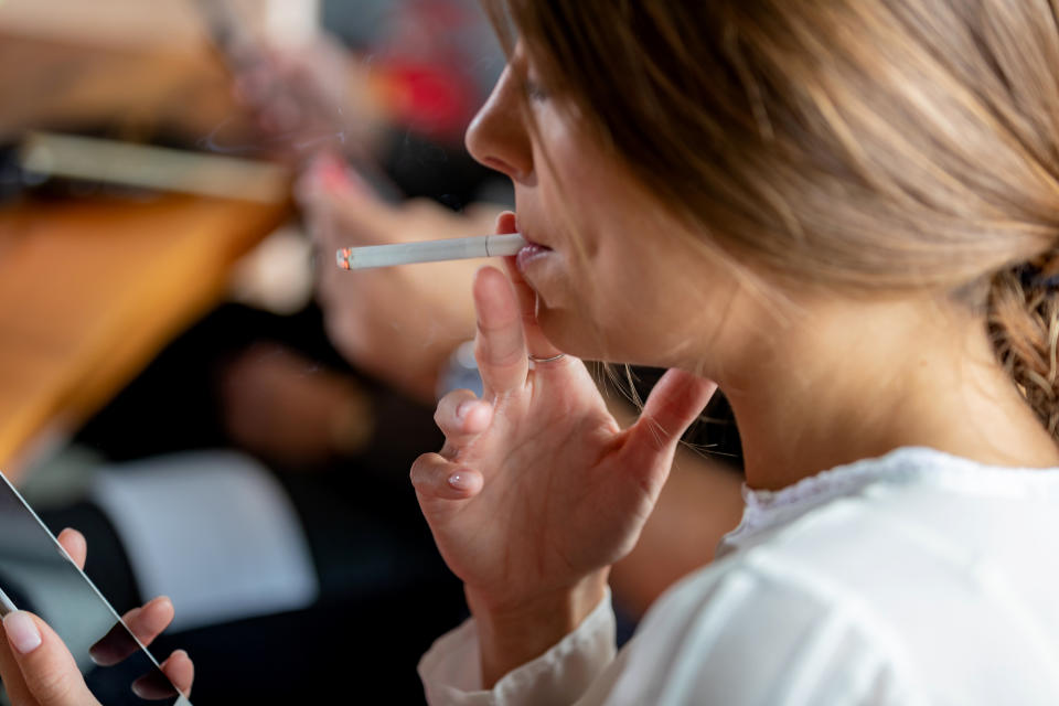 Businesswoman looking at smartphone, smoking cigarette on lunch break in sushi bar