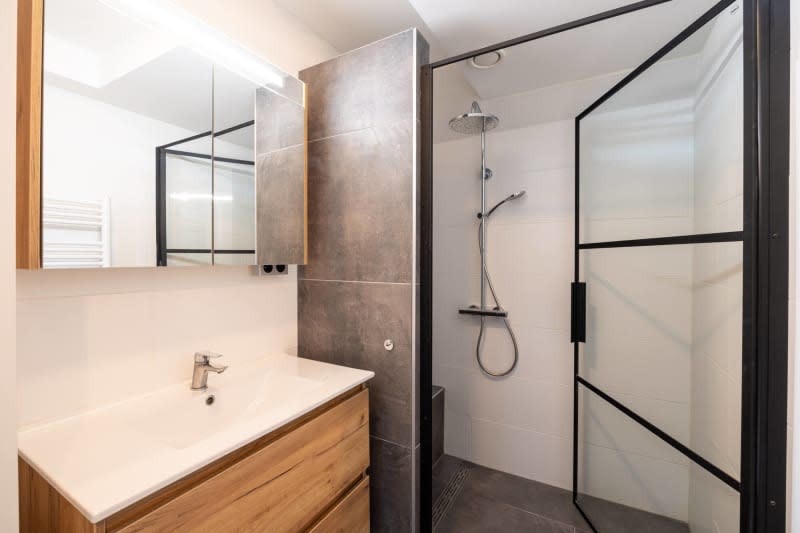 Modern bathroom with walk in shower, large glass door, wood vanity and gray tile