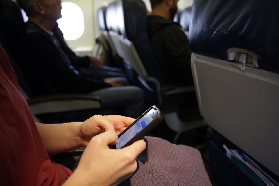 FILE - In this Oct. 31, 2013, file photo, a passenger checks her cell phone before a flight in Boston. The Federal Communications Commission might be ready to permit cellphone calls in flight. Old concerns about electronics being a danger to airplane navigation have been debunked. And carriers could make some extra cash charging passengers to call a loved one from 35,000 feet. But that extra money might not be worth the backlash from fliers who view overly-chatty neighbors as another inconvenience to go along with smaller seats and stuffed overhead bins. (AP Photo/Matt Slocum, File)