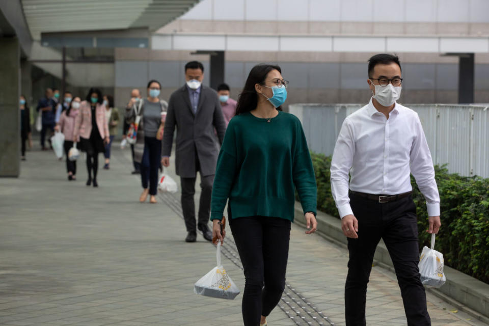 Office workers wearing masks carry take-out lunch orders while walking towards in Admiralty, Hong Kong, on Mar. 2, 2020. | Paul Yeung—Bloomberg/Getty Images
