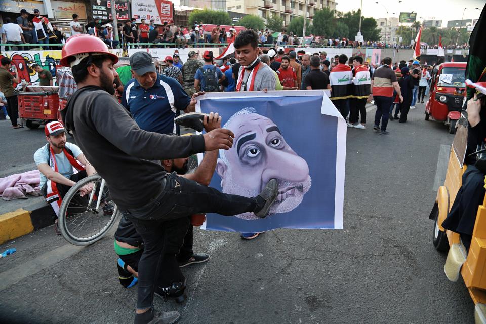 Protesters hit a poster showing Iraqi Prime Minister Adel Abdel-Mahdi with shoes during ongoing anti-government protests in Baghdad, Iraq, Sunday, Nov. 3, 2019. (AP Photo)