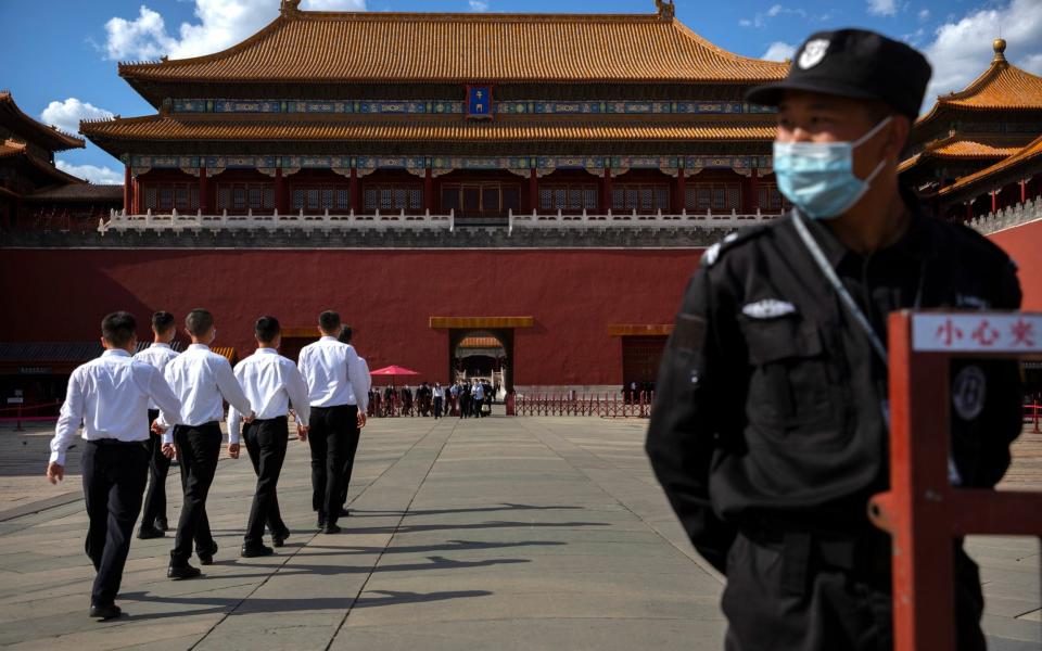 A security officer stands guard as plainclothes personnel march in formation outside the entrance to the Forbidden City in Beijing - AP Photo/Mark Schiefelbein