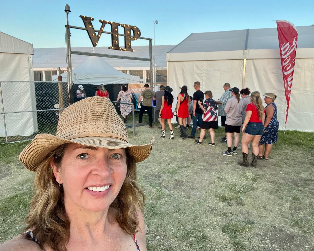 The writer in a cowboy hat smiling in front of a "VIP" sign above a tent with people lined up to enter it