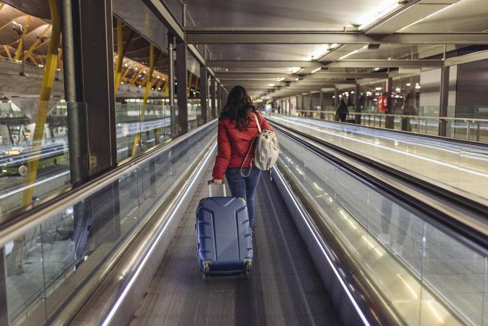 Young woman walking in the airport terminal&#39;s hovering walkway with her suitcases