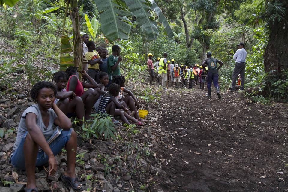 In this April 10, 2012 photo, people watch as workers build a road through the mountains that will lead to an exploratory drill site in the department of Trou Du Nord, Haiti. Haiti's land may yet hold the solution to centuries of poverty: there is gold hidden in its hills, and silver and copper too. Now, two mining companies are drilling around the clock to determine how to get those metals out, and how much it might cost. (AP Photo/Dieu Nalio Chery)