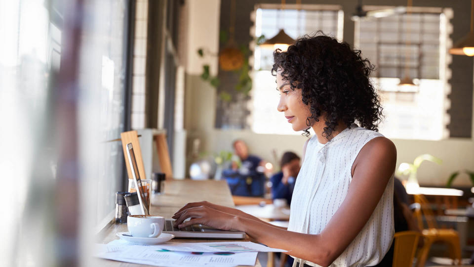 Businesswoman By Window Working On Laptop In Coffee Shop.