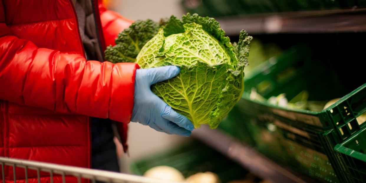 A person picking up cabbage while wearing protective gloves at a supermarket.