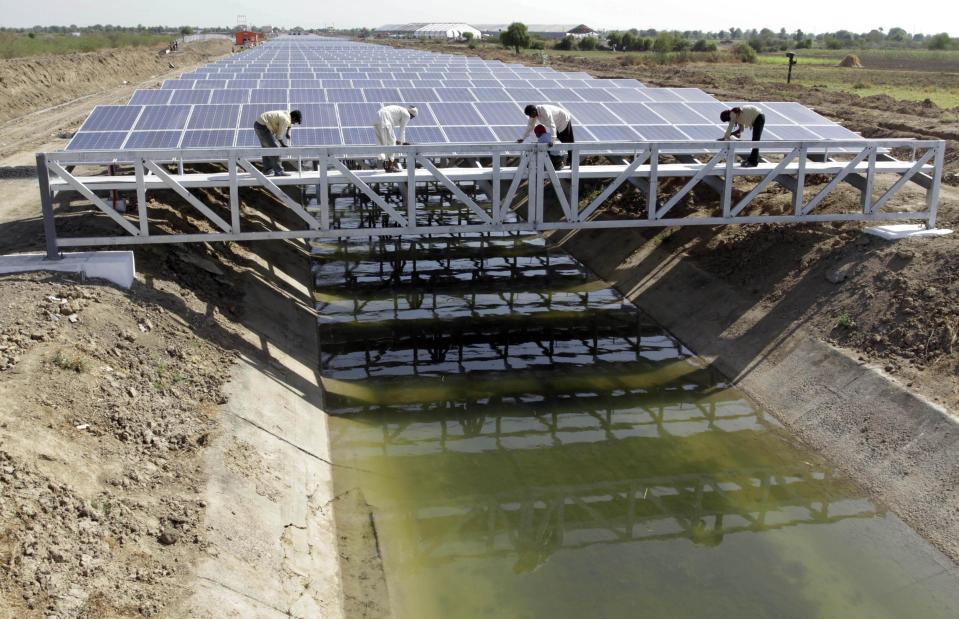 FILE - Indian workers give finishing touches to installed solar panels covering the Narmada canal ahead of its inauguration at Chandrasan village, near Ahmadabad, India, April 22, 2012. The Gila River Indian Community recently signed an agreement with the U.S. Army Corps of Engineers to put solar panels over a stretch of irrigation canal on their land south of Phoenix, similar to what India has done. (AP Photo/Ajit Solanki, File)