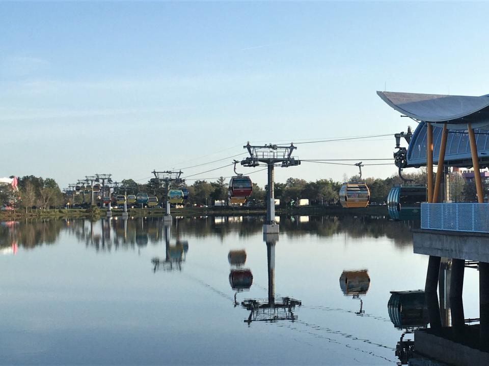 disney skyliner gondolas going over a lagoon of water at disney world