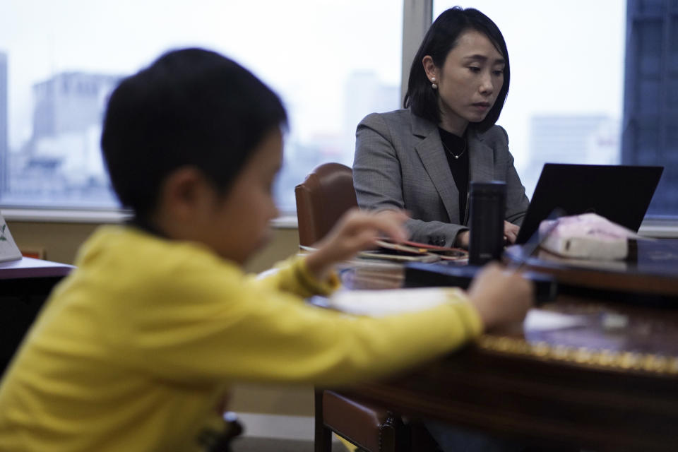 Sachiko Aoki, an employee of the staffing services company Pasona Inc., works as her son does his homework at the company's headquarters Monday, March 2, 2020, in Tokyo. Many Japanese schools were shut down Monday and spring holidays began unexpectedly early for children as part of a government-led measure to prevent further escalation of the coronavirus. The measure is a big burden and a headache for working mothers, especially those with small children or disabilities. (AP Photo/Eugene Hoshiko)