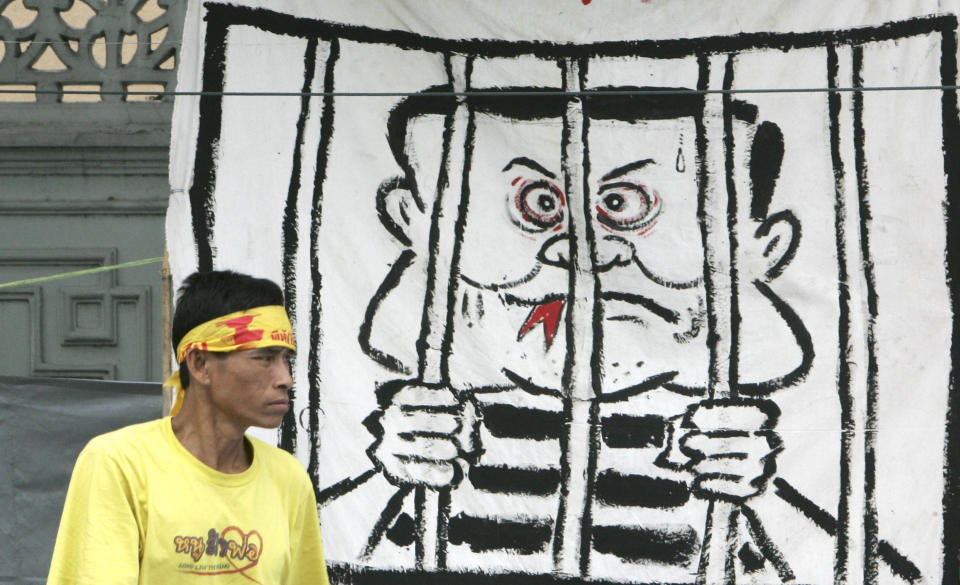 FILE - An anti government protester walks past a poster depicting ousted Thai Prime Minister Thaksin Shinawatra behind bars outside Government House in Bangkok, Thailand, Thursday July 3, 2008. Thaksin Shinawatra, a controversial former Prime Minister of Thailand, made his dramatic return to Thailand last year after nearly a decade of self-imposed exile. Although he was detained in a hospital and never appeared in the public eye for six months after his arrival, his presence in the country alone brings a turmoil into Thai politics like no other politician could ever achieve. (AP Photo/Sakchai Lalit, File)