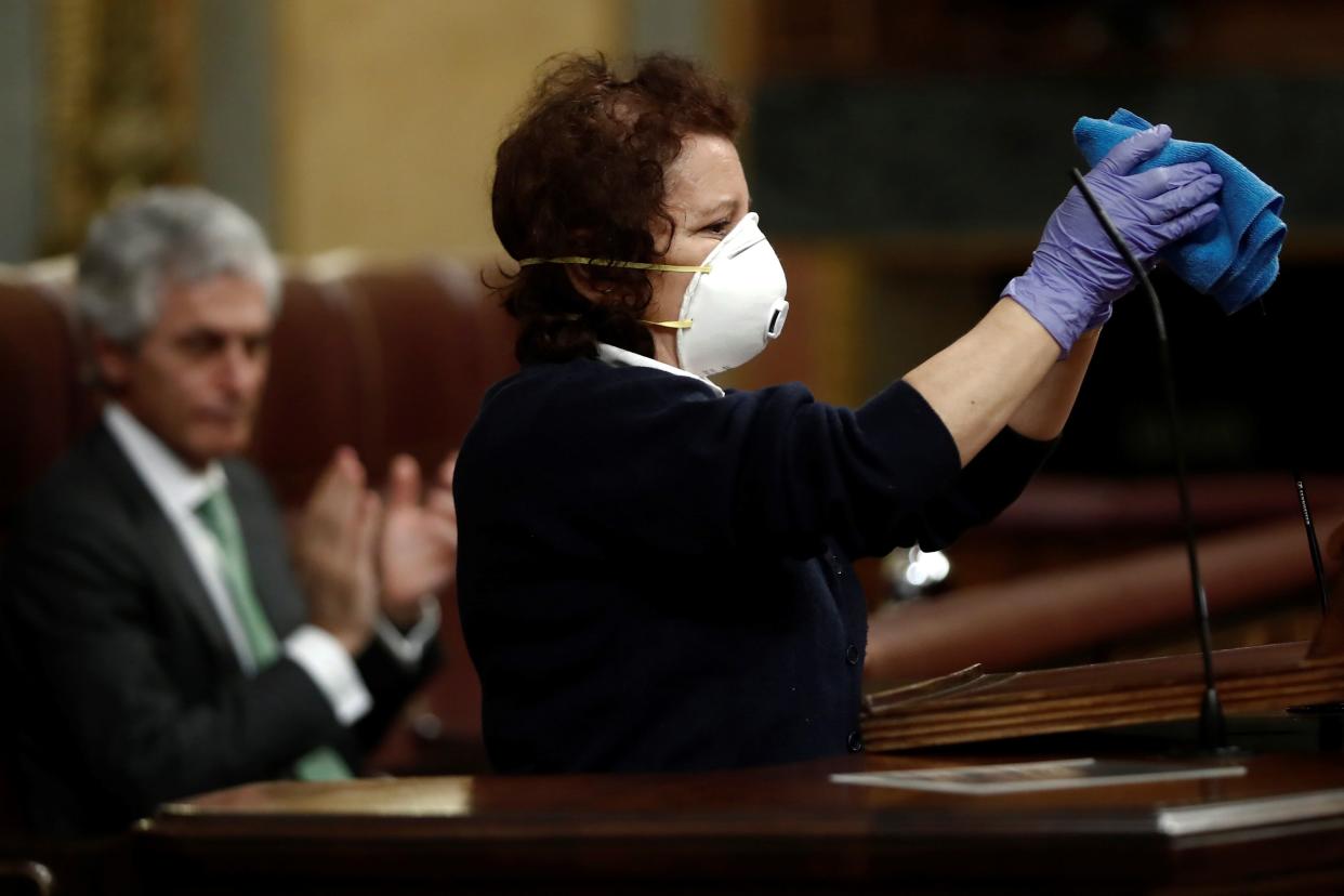 A worker cleans the microphones in a nearly empty parliament while the majority of lawmakers follow the session online before a vote to approve the extension of the national lockdown in Madrid, Spain,  on Wednesday, March 25, 2020. Spain has released new figures of the official death toll in Spain because of the coronavirus, surpassing China's death toll.