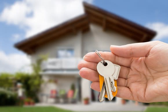 Hand holding keys with a home in the background