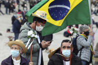 A pilgrim wearing a face mask checks his phone while another holds a Brazilian flag while waiting for the start of the religious ceremonies at the Catholic shrine in Fatima, Portugal, Thursday, May 13, 2021. In view of the coronavirus pandemic, the shrine has limited to 7,500 the number of pilgrims that can be present during this year's May 12 and 13 celebrations usually attended by hundreds of thousands. (AP Photo/Ana Brigida)