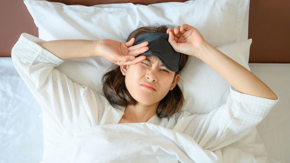 Woman waking up, pulling an eye mask up to let light in