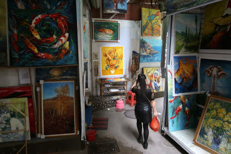 A woman walks through an alley surrounded by paintings on walls at Dafen Oil Painting Village in Shenzhen, Guangdong province, China December 5, 2018. REUTERS/Thomas Suen/Files