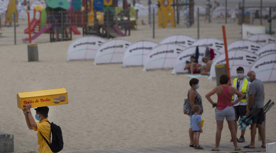 A vendor, left, carries a box selling Boules de Berlin at the Belgian seaside resort of Blankenberge, Belgium, Tuesday, Aug. 11, 2020. A skirmish took place on the beach on Saturday, Aug. 8, 2020 which resulted in two coastal communities banning day trippers from the city. (AP Photo/Virginia Mayo)