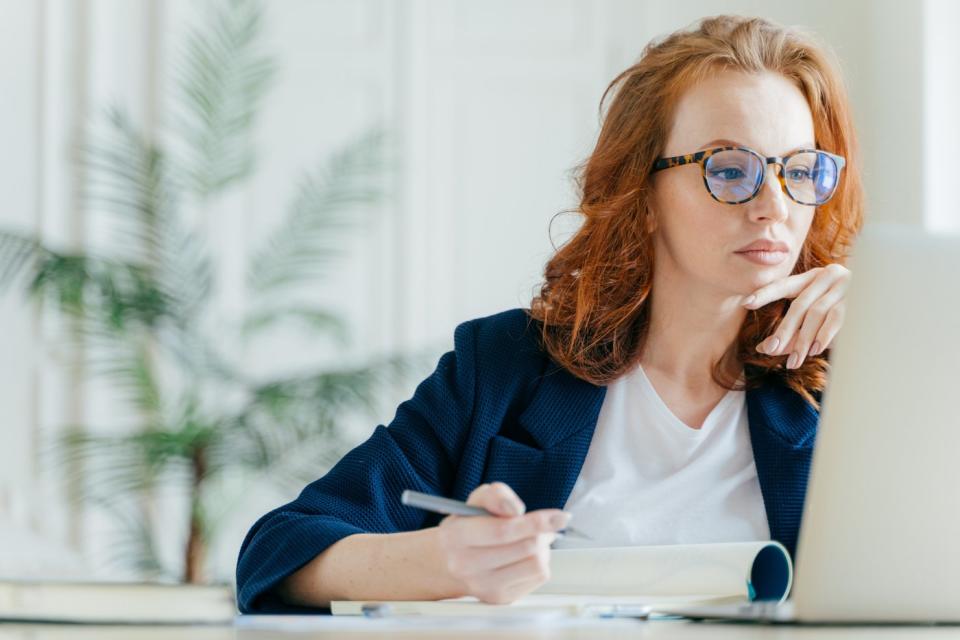 An investor looks at something on a laptop screen while taking notes.