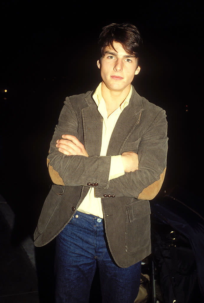 Tom Cruise in a striped blazer and jeans, standing with crossed arms