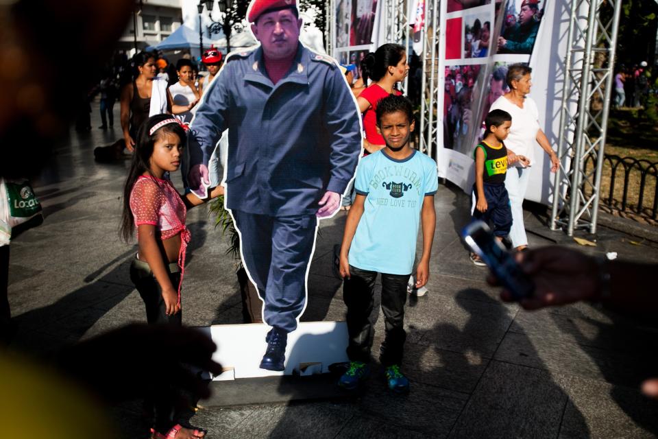 Children pose with a life-size cardboard cutout of Venezuela's late President Hugo Chavez while waiting for the arrival of President Nicolas Maduro in Bolivar Square for a rally to commemorate International Women's Day in Caracas, Venezuela, Saturday, March 8, 2014. (AP Photo/Alejandro Cegarra)