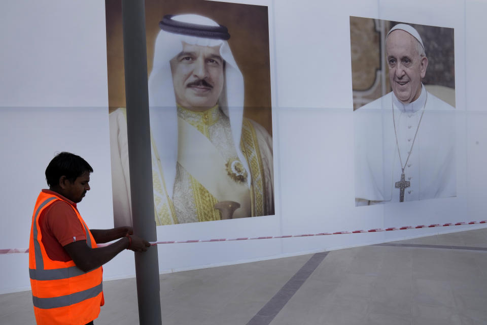 Un trabajador coloca una barra ante los retratos del papa Francisco, a la derecha, y el rey de Bahréin, Hamad bin Isa Al Khalifa, a la izquierda, ante la Catedral de Nuestra Señora de Arabia, donde el papa asistirá a una misa en Manama, Bahréin, el miércoles 2 de noviembre de 2022. (AP Foto/Hussein Malla)