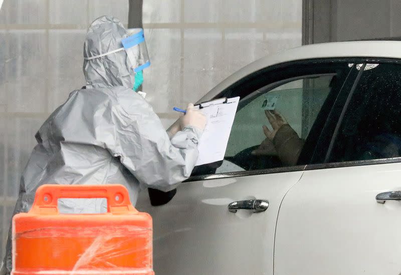 FILE PHOTO: A person holds up their ID as a worker in protective clothing gathers information from people that want to get tested, at Glen Island Park in New Rochelle