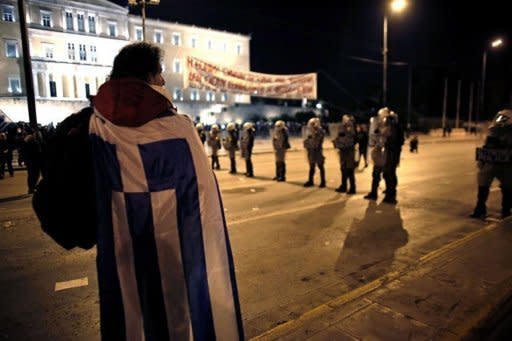 A protester stands facing riot police outside the Greek parliament during a demonstration against new austerity measures in Athens. A huge eurozone rescue package agreed saves Greece from default, keeps it in the single currency bloc under strict controls but markets are sceptical and Greek unions are calling fresh protests