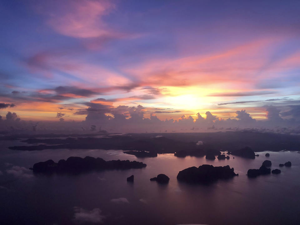 The sun sets over outlying islands as a plane prepares to land on the resort island of Phuket, Thailand on Wednesday, May 22, 2019. Thailand plans to allow vaccinated foreigners to visit the southern resort island of Phuket without quarantining on arrival in a step toward reviving the country's big but battered tourism industry. (AP Photo/Adam Schreck)