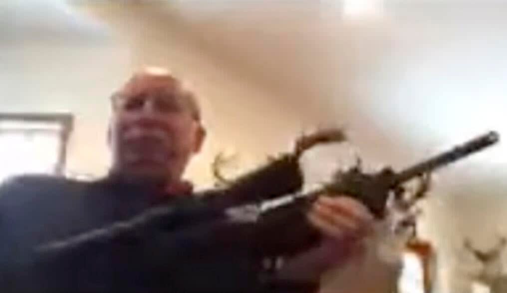 Ron Clous holds gun during county meeting. (YouTube)