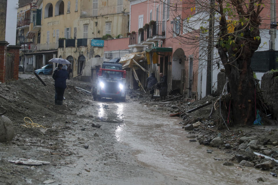 A caterpillar removes mud from a flooded road after heavy rainfall triggered landslides that collapsed buildings and left as many as 12 people missing, in Casamicciola, on the southern Italian island of Ischia, Saturday, Nov. 26, 2022. Firefighters are working on rescue efforts as reinforcements are being sent from nearby Naples, but are encountering difficulties in reaching the island either by motorboat or helicopter due to the weather. (AP Photo/Salvatore Laporta)