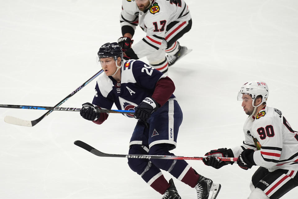 Colorado Avalanche center Nathan MacKinnon, center, passes the puck while driving between Chicago Blackhawks center Tyler Johnson, front, and left wing Nick Foligno during the third period of an NHL hockey game Monday, March 4, 2024, in Denver. (AP Photo/David Zalubowski)