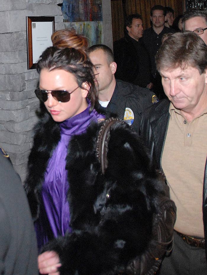 A young adult Britney, with dark hair, walking outside with her father behind her