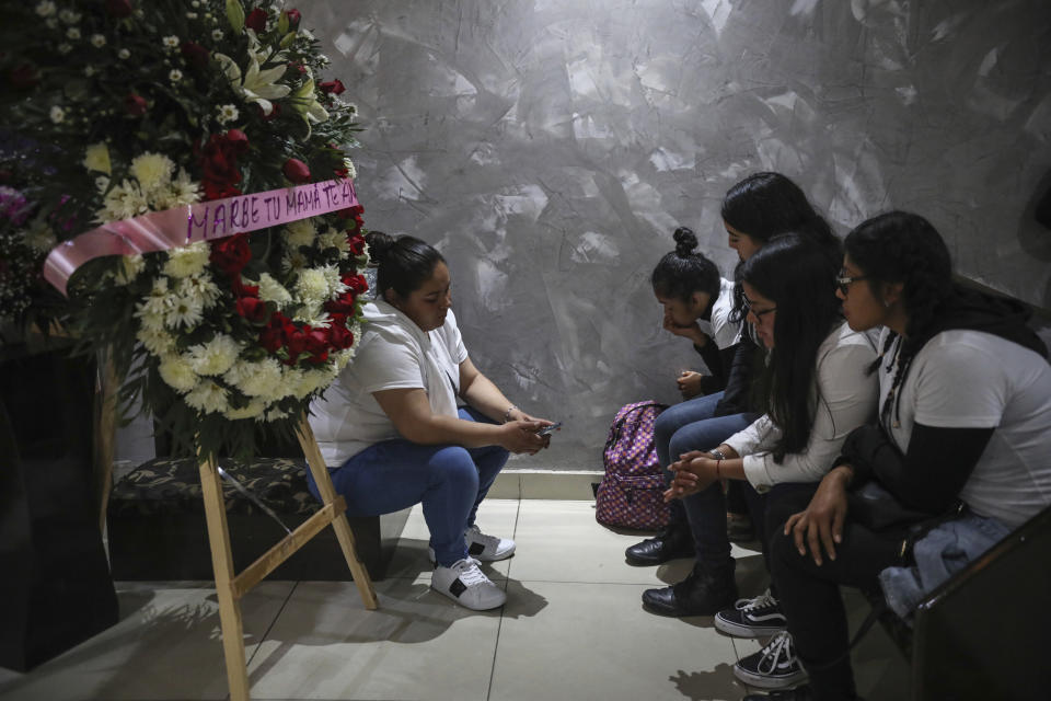 Friends of slain woman Marbella Valdez sit together by a floral arrangement that reads in Spanish "Marbe, your mom loves you," near her coffin during her wake at a funeral home in Tijuana, Mexico, Thursday, Feb. 13, 2020. When the law student’s body was found at a garbage dump in Tijuana, the man who was obsessed with her demanded police solve the case, attended her funeral, and a week later was arrested and charged with her murder. The man, identified by Mexican rules only by his first name, Juan, has insisted on his innocence. (AP Photo/Emilio Espejel)