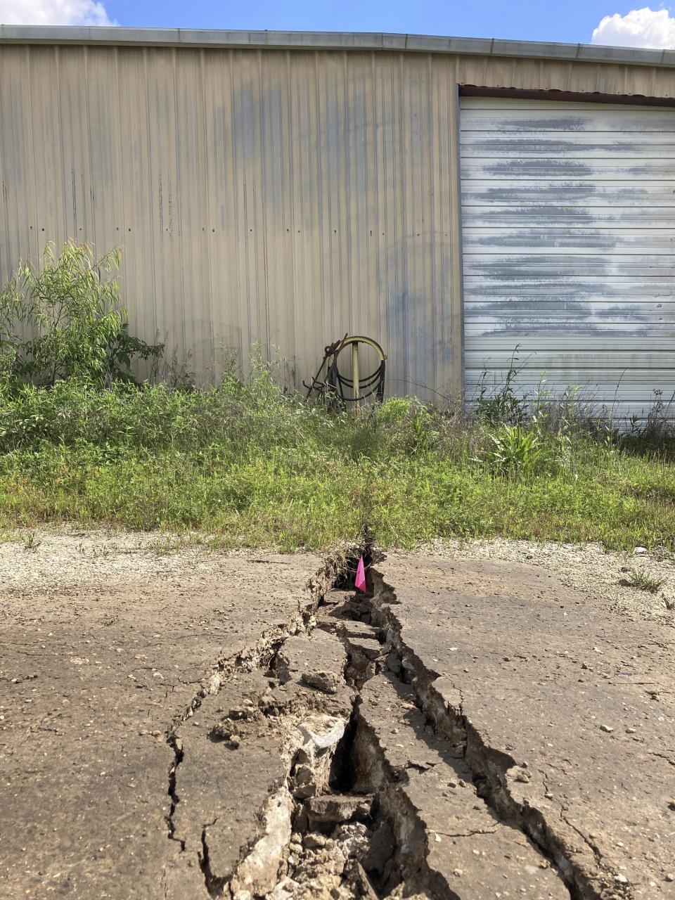 Cracks and other damage caused by a sinkhole in Daisetta, Texas, can be seen around a shuttered oil and gas waste well business located next to the opening in the ground, Tuesday, April 11, 2023. Earlier this month, Daisetta officials announced the sinkhole, which had first emerged in 2008 but had been dormant since then, had started to again expand. Officials say they're monitoring the new growth and keeping residents informed. (AP Photo/Juan A. Lozano)