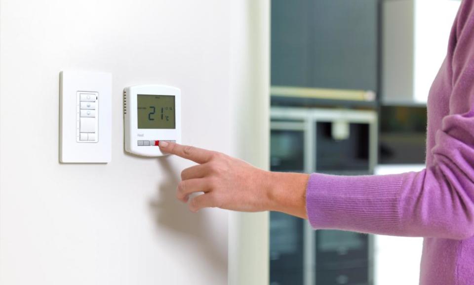 A woman adjusting a home thermostat.