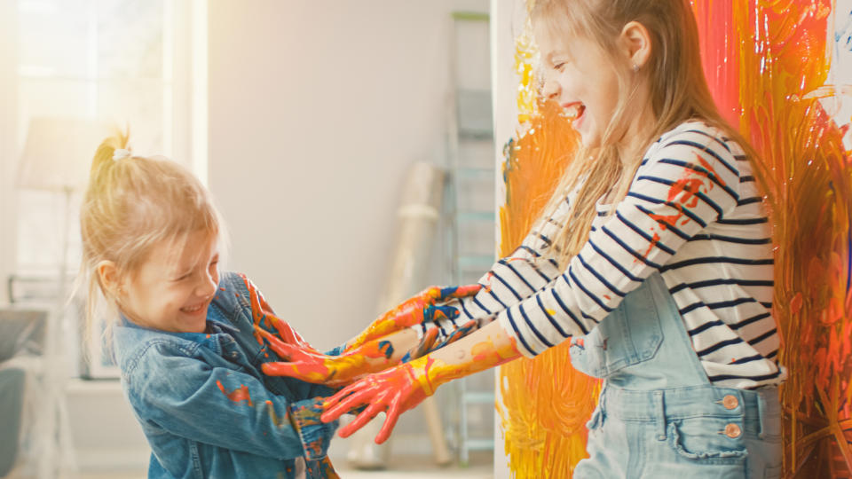 Two Fun Little Sisters Play and Fool Around with Their Hands Dipped in Colorful Paint. They are Happy and Laugh. Sisterhood Goals. Redecoration at Home.